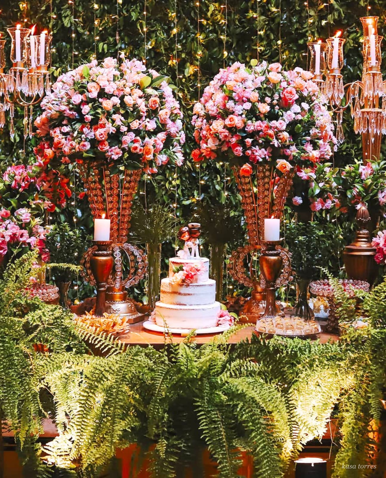 Mesa de bolo de casamento romântica com vasos altos de rosas, candelabros de cobre e samambaias — Kasa Torres